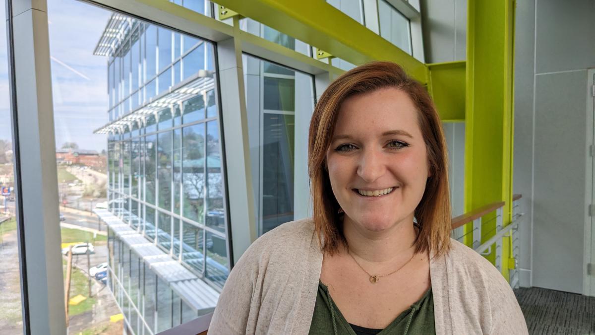 Disability Accommodations Specialist Kelly Woodbridge smiles as she stands in a glass-encased bridge on a sunny day in South Bethlehem near her new office in Lehigh Human Resources. 