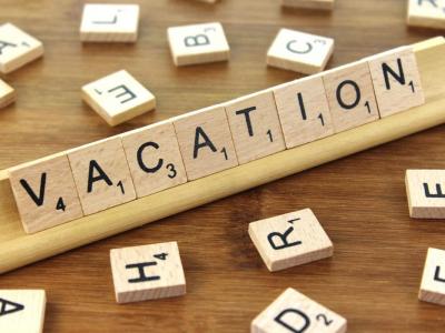 Wooden tiles each with a single letter spelling out the word vacation with more wooden tiles scattered around.