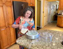 Susan Woodhouse, a professor in the College of Education, smiles as she stands in her kitchen pouring liquid into the yogurt maker she paid for with her BeWell gift cards.