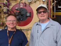Coworkers Marshall Pysher and Dave Novogratz smile as they stand in front of Boiler #2 in the Lehigh Boiler House