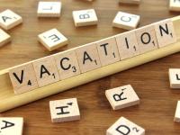 Wooden tiles each with a single letter spelling out the word vacation with more wooden tiles scattered around.