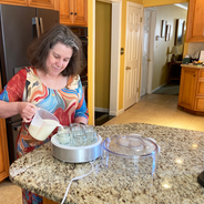 Susan Woodhouse, a professor in the College of Education, smiles as she stands in her kitchen pouring liquid into the yogurt maker she paid for with her BeWell gift cards.
