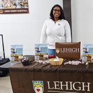 Human Resources Assistant Tashia Winn smiles as she stands behind a table at Stabler Arena. Tashia recently represented Lehigh at an event to promote job opportunities at Lehigh University
